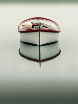 A small white boat with red trim floats on perfectly still water, its reflection forming a serene, symmetrical scene. (Colour image)