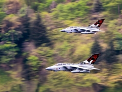 Two grey fighter jets fly in tight formation at low level over blurred green terrain, with bold tail markings celebrating the 70th anniversary of the Dambusters Squadron. (Colour image)