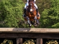 High‑action sports photograph capturing a rider and horse mid‑jump over a wooden cross‑country fence.