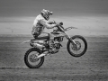 Dynamic off‑road biking image showing a motocross rider accelerating over rough terrain with the front wheel raised.