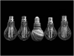 A horizontal row of five bulbs sits against a black background; four are clear with visible filaments, while the central bulb is opaque and filled with textured layers of sand