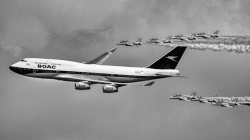 A large passenger aircraft painted in a retro BOAC livery flies in close formation with several smaller jet aircraft, each leaving smoke trails as they sweep through a cloudy sky in a black‑and‑white composition